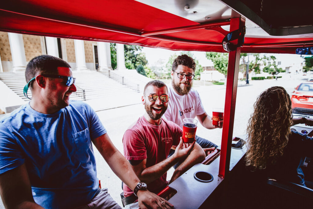 Group of friends enjoying drinks on a red trolley with a scenic view in the background.