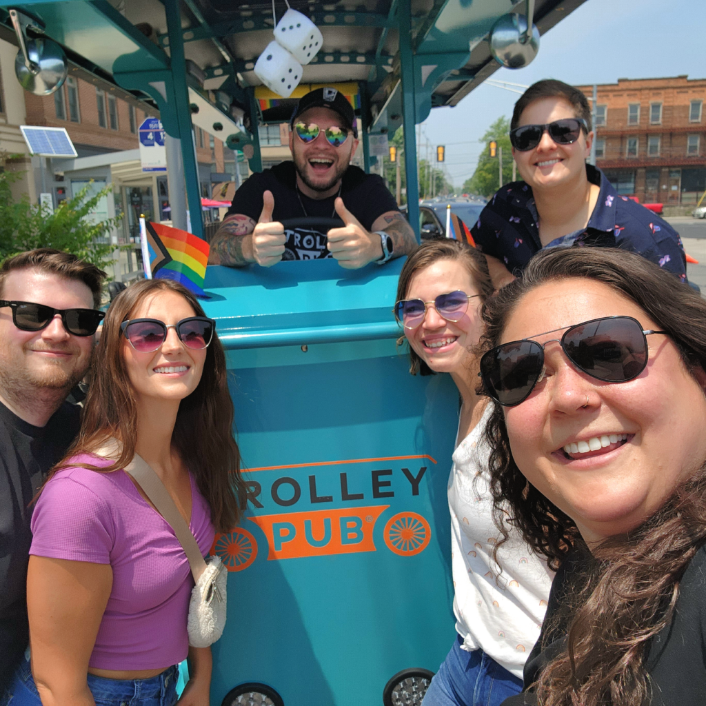 Group of people in front of a trolley pub during a sunny day, with a colorful diner sign in the background.