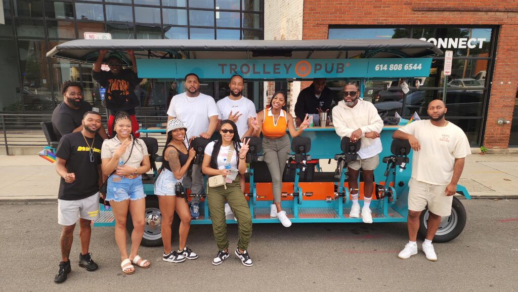 Group of friends posing in front of a Trolley Pub vehicle on a street.