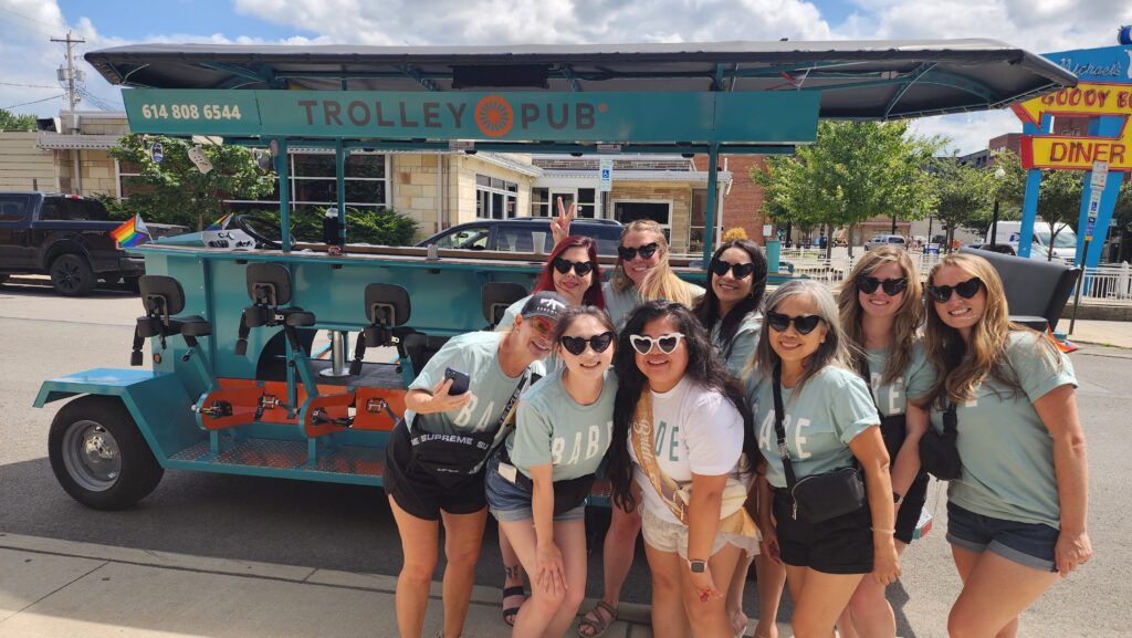 A group of women posing in front of a trolley pub with a colorful background and a diner sign.