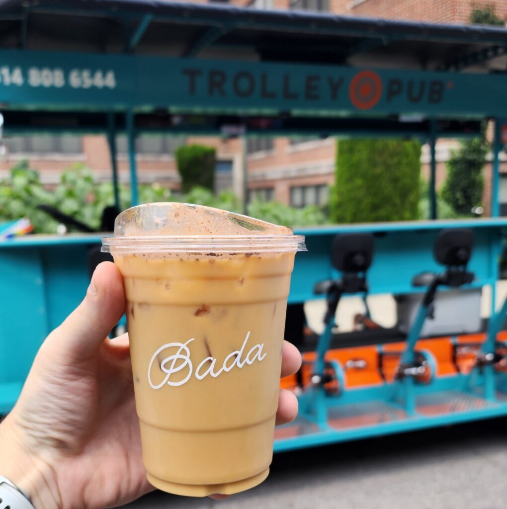 Hand holding an iced coffee in front of a blue trolley pub.