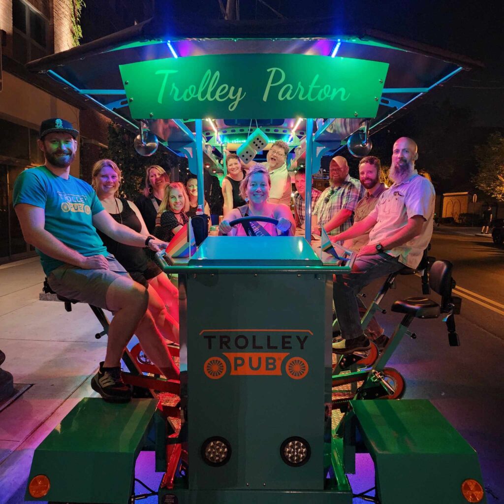 A group of people smiling and posing in front of a Trolley Pub in Columbus, Ohio, with a mural in the background.