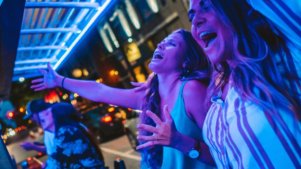 People enjoying nightlife with neon lights and city backdrop.