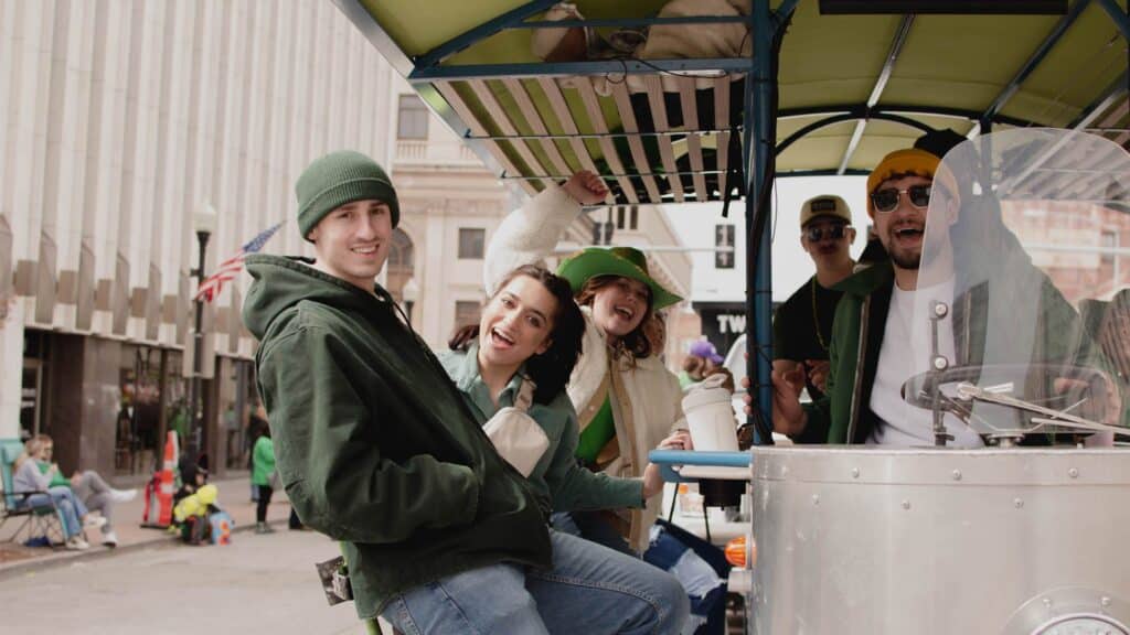 A group of people wearing green outfits on a festive pedicab on a city street.