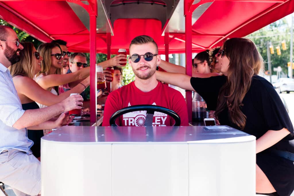 Group of people sitting at a pedal-powered bar table with red canopy.