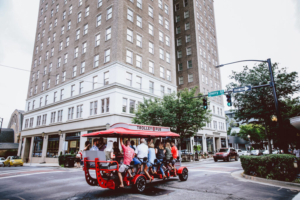 A red pedal-powered trolley pub with passengers on a city street.