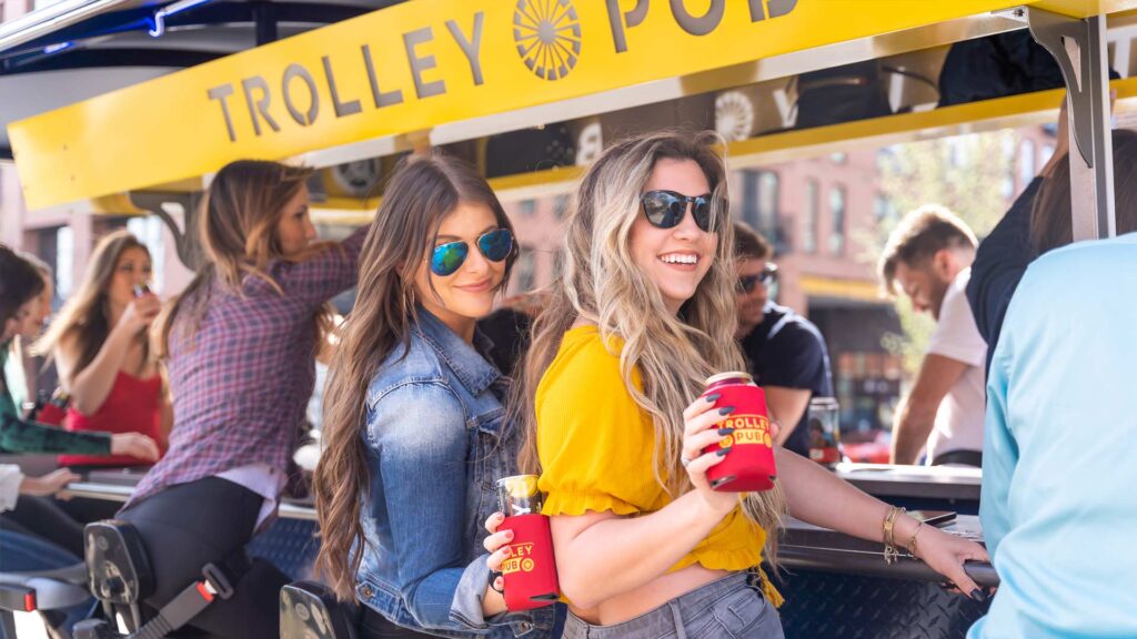 Group enjoying drinks on a trolley pub ride in the city during a sunny day, featuring friends socializing and smiling.